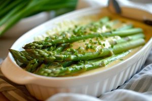 Oven baked asparagus with cheese and chives, serve in a white baking dish, close up side view